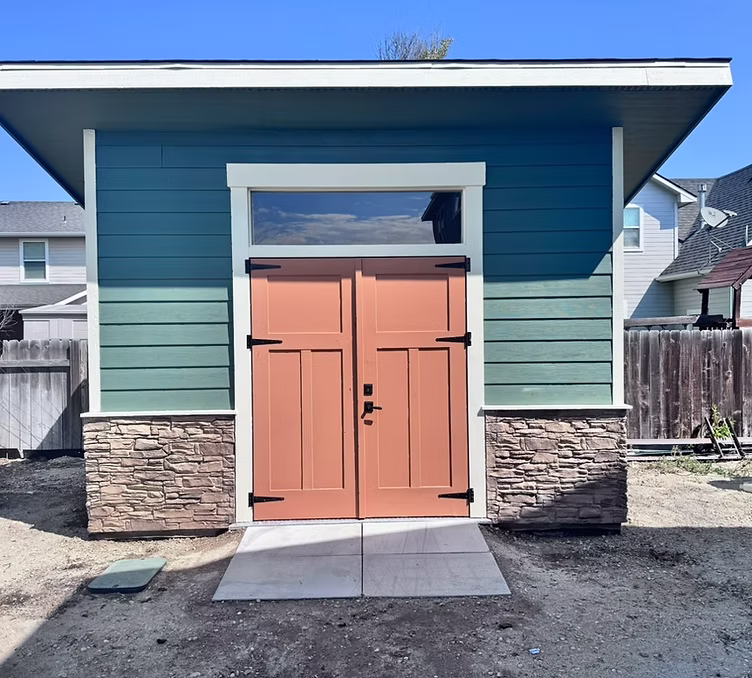 A custom craftsman-style shed on a stone-veneer base — the kind of utility building that can sit over a vault entry.